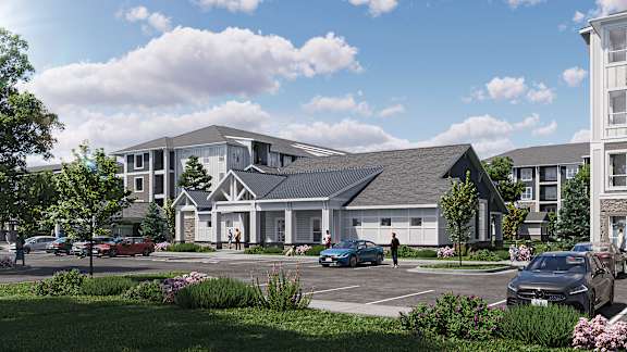 A modern house with a grey roof and white walls is surrounded by a grassy area and a parking lot with cars.