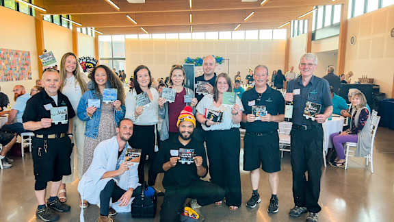A group of people are gathered in a room, some holding books.