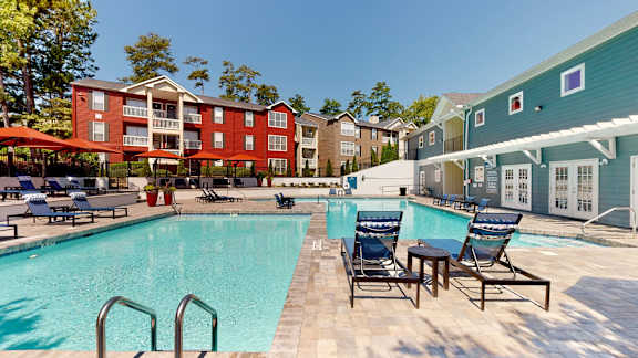 A pool surrounded by chairs and umbrellas with a building in the background.