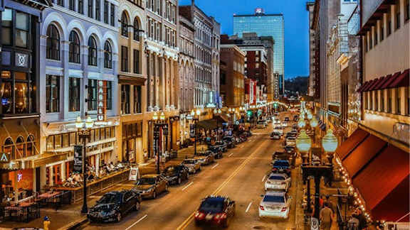A city street at night with cars parked on the side and buildings on both sides.