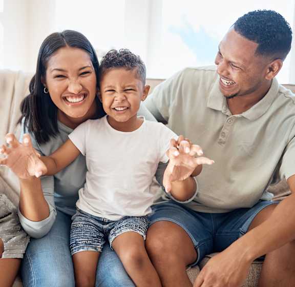 a family sitting on a couch smiling and waving to the camera