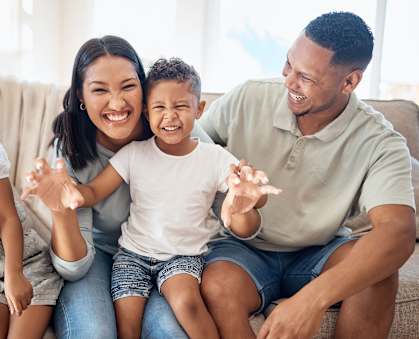 a family sitting on a couch smiling and waving to the camera