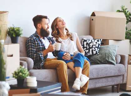 A couple is sitting on a couch surrounded by moving boxes.