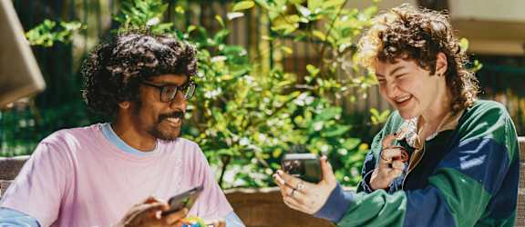 Two people sitting at a table, one holding a phone and the other holding a camera.
