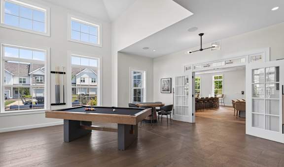 Pool table centered in a bright game room with tall windows and lounge seating.