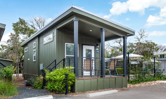 a green tiny house with a porch with two chairs on it