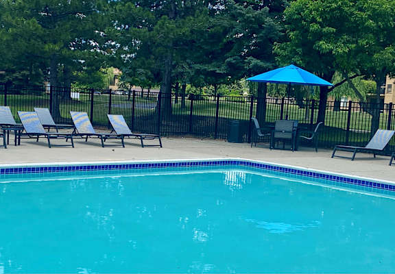 A pool surrounded by a black fence and chairs.