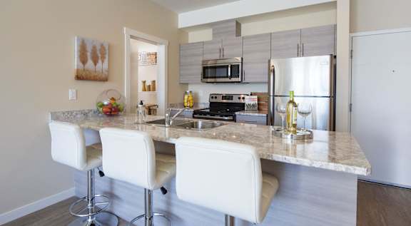 A kitchen with a granite countertop and white bar stools.