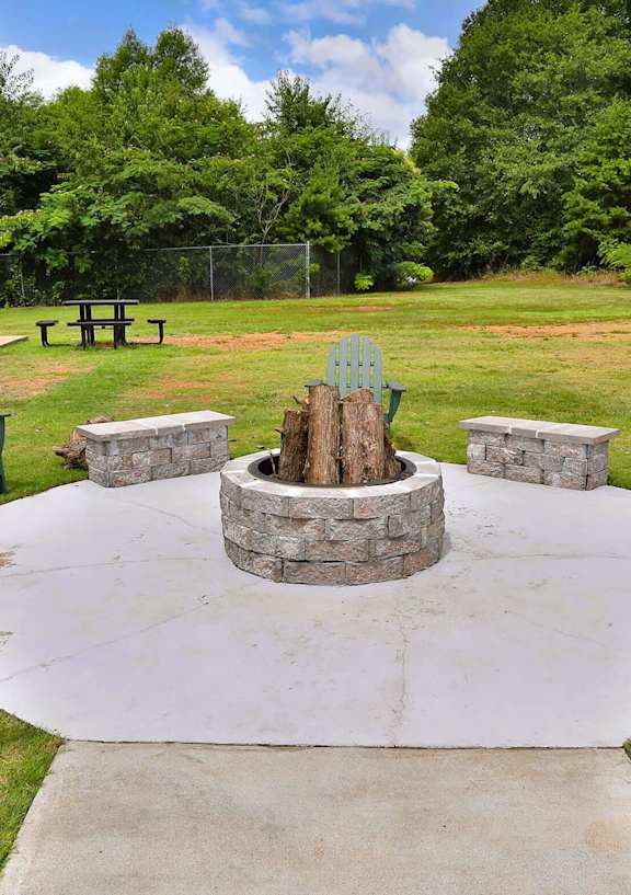 A fire pit surrounded by green chairs in a park.