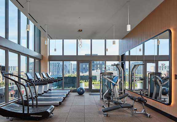 a gym with treadmills and weights with a view of the city