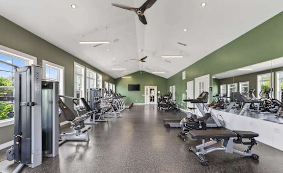 Fitness studio with strength machines, benches, free weights, mirrors, and ceiling fans.