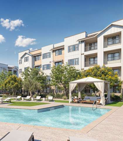 A swimming pool surrounded by lounge chairs and umbrellas in front of apartment buildings at Orchard Springs 55+ Apartment, Surprise, AZ, 85374