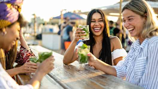 Four people are sitting at a table, laughing and enjoying drinks.