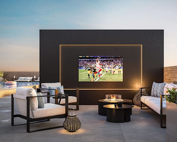 A modern outdoor living space with a television, seating, and a fire pit.