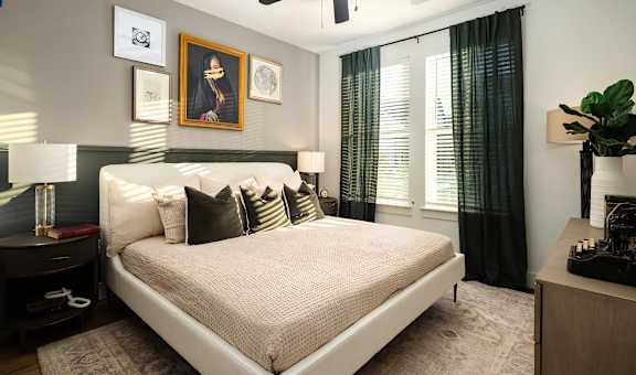 A bedroom with a large bed, a nightstand with a lamp, and a plant on a table.