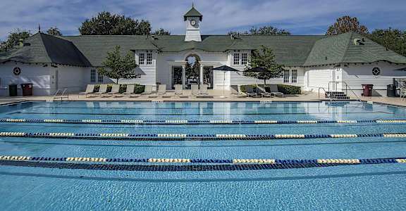A large swimming pool in front of a white building with a green roof.