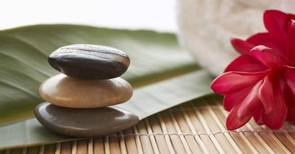 a stack of rocks on a bamboo mat next to a red flower