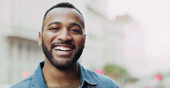 A man with a beard is wearing a denim shirt and a brown turtleneck.