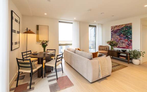 Fully furnished open-plan living and dining room in a one-bedroom apartment with floor-to-ceiling windows.