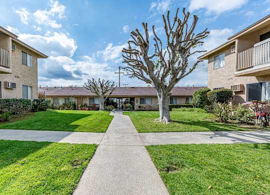 a walkway between two apartment buildings with grass and trees at Colima Terrace Apts, Rowland Heights, 91748