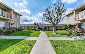a walkway between two apartment buildings with grass and trees at Colima Terrace Apts, Rowland Heights, 91748