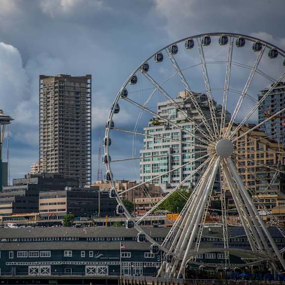 A ferris wheel is in the foreground of a city skyline with the Space Needle in the background.