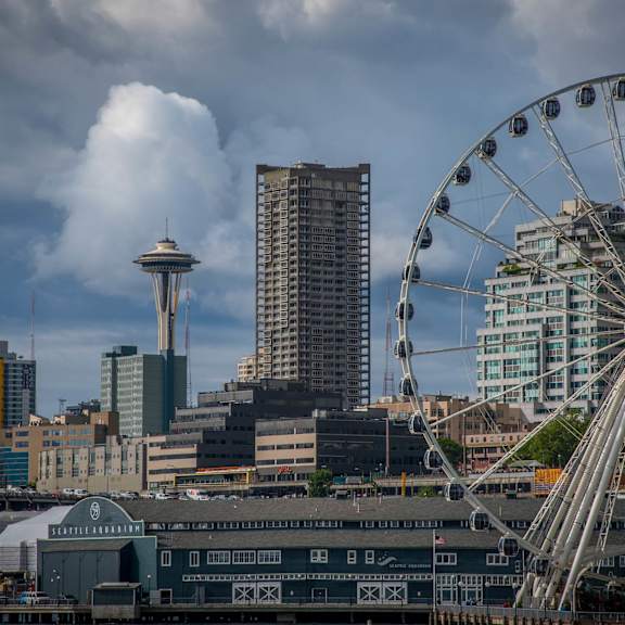 A ferris wheel is in the foreground of a city skyline with the Space Needle in the background.