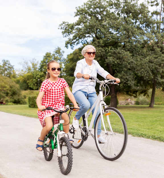 A woman and a girl are riding a bicycle in a park.