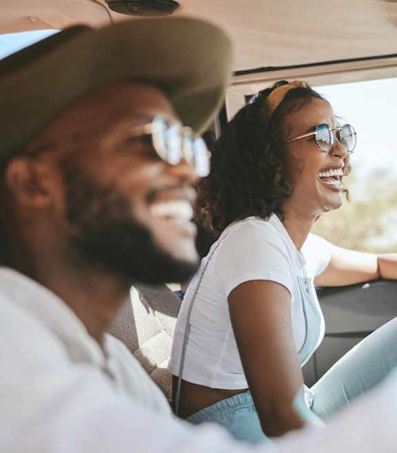 A man and a woman are sitting in a car, both wearing sunglasses and enjoying a sunny day out.