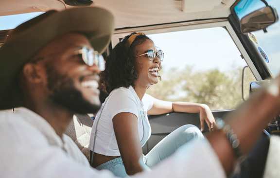 A man and a woman are sitting in a car, both wearing sunglasses and enjoying a sunny day out.