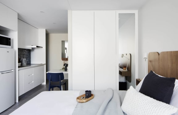 a bedroom with a white bed and a kitchen in the background