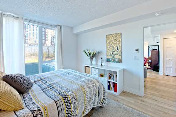 A bedroom with a bed, a window with curtains, a painting on the wall, and a bookshelf with books.