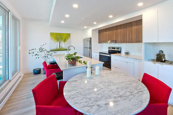 A modern kitchen with a marble table and red chairs.