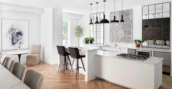 A modern kitchen with a white island and black chairs.