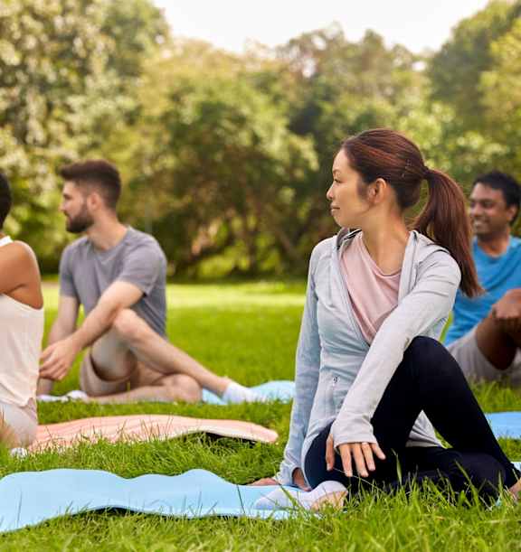 A group of people are sitting on yoga mats in a park.