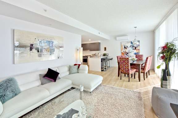 A white couch with a grey pillow is in the middle of a room with a painting on the wall.