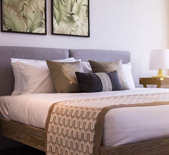 A bed with a grey headboard and a white comforter with a patterned pillow case.