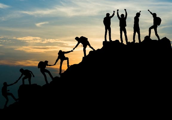 silhouettes of people hiking up a mountain with their hands in the air