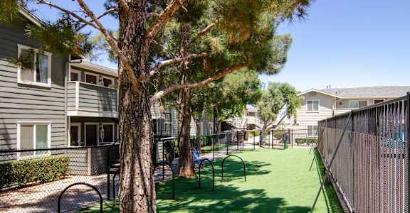 a fenced in dog park with trees and benches at Aspire High Desert Apartments, Victorville, 92392