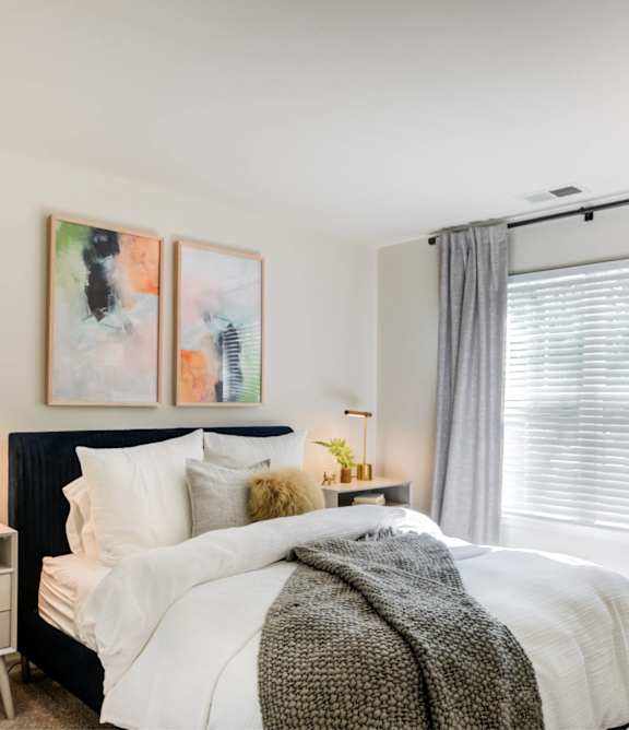 A bedroom with a large bed, a nightstand with a lamp, and a painting on the wall.