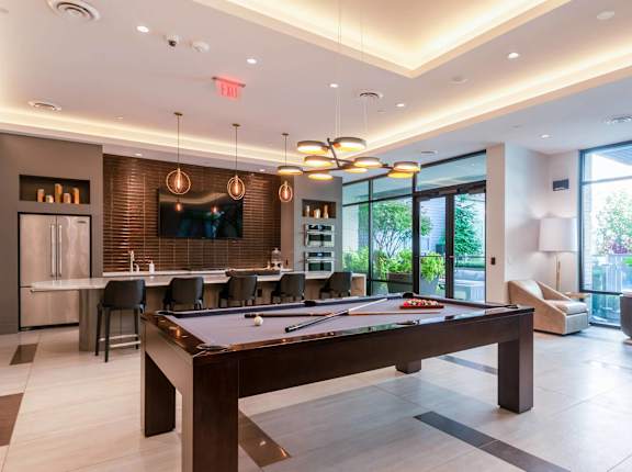 A pool table is in the middle of a room with a bar and a television.