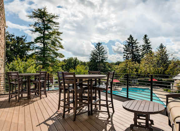 A wooden deck with a table and chairs overlooking a pool.