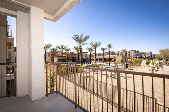 A balcony with a railing overlooks a pool and palm trees.