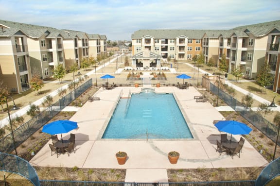 an aerial view of a swimming pool with umbrellas and apartments in the background at Mariposa at Bay Colony, Dickinson, TX 77539
