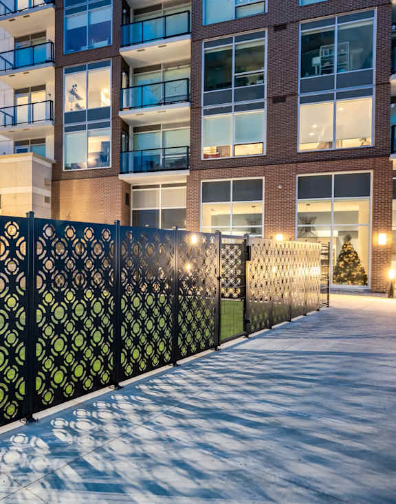 A black metal fence with a lattice pattern separates a sidewalk from a building.