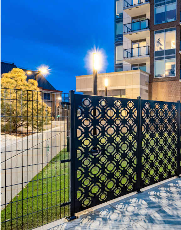 A black metal fence with a lattice pattern separates a sidewalk from a building.