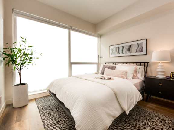A bedroom with a large bed, a plant, and a painting on the wall.