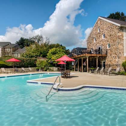 A swimming pool with a stone building and red umbrellas in the background.