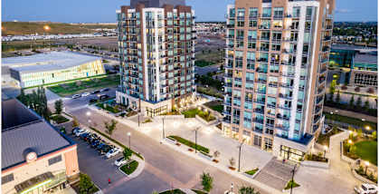 Two modern high-rise buildings are surrounded by a parking lot and other buildings.
