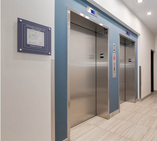 Two elevators in a hallway with a plaque on the wall.